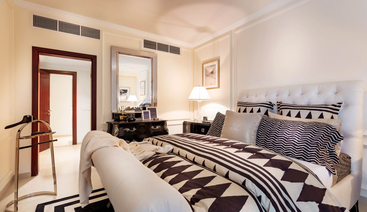 A hotel bedroom with a patterned throw, crisp linen and a padded headboard