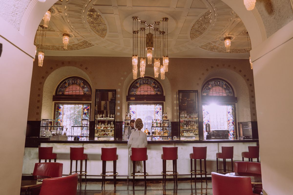 An ornate bar with crystal chandeliers and red bar stools