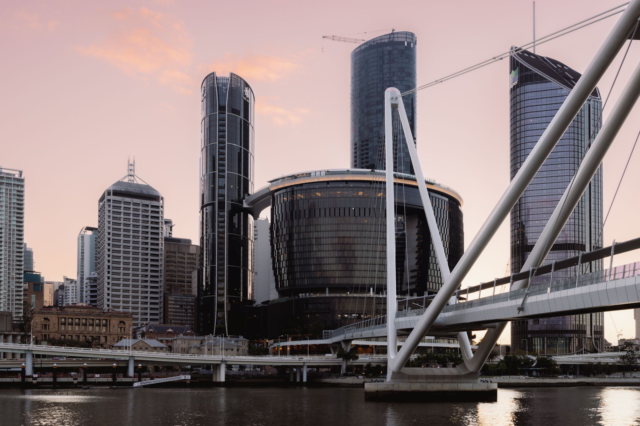 Brisbane's city towers rising behind the Kurilpa Bridge at dusk