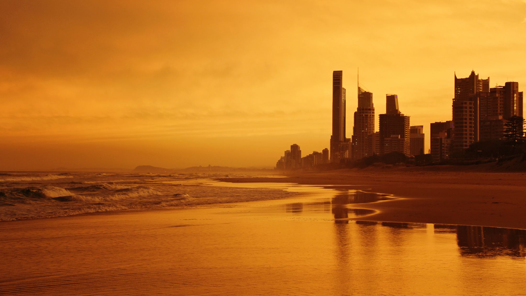 The Gold Coast skyline at sunset, seen from a wide, empty beach