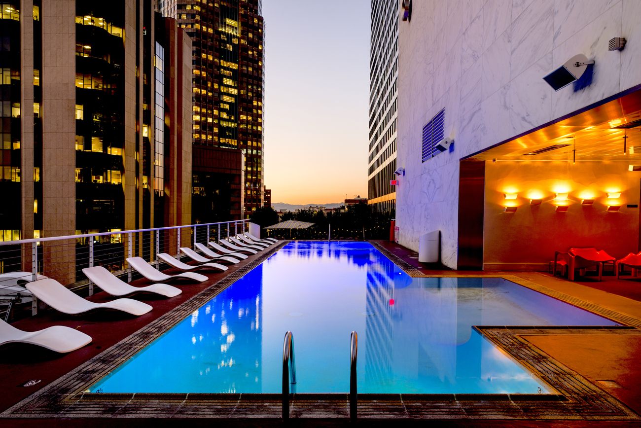 A lit swimming pool lined with white sun loungers at dusk