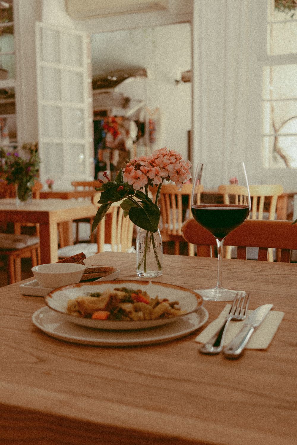 A restaurant table set with a vase of flowers and a glass of wine