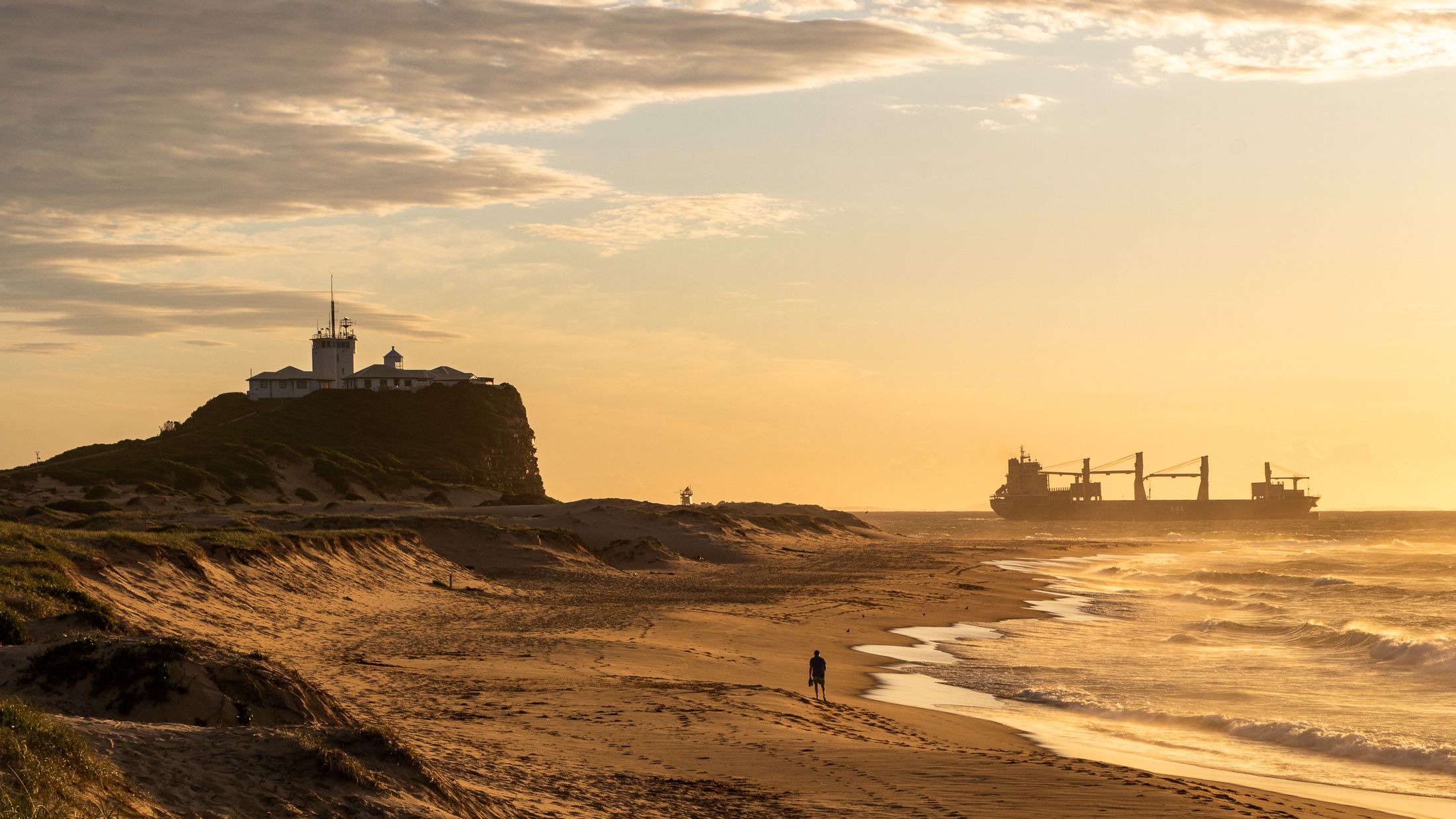 Nobbys Beach and its lighthouse in Newcastle at sunset, with a ship waiting offshore